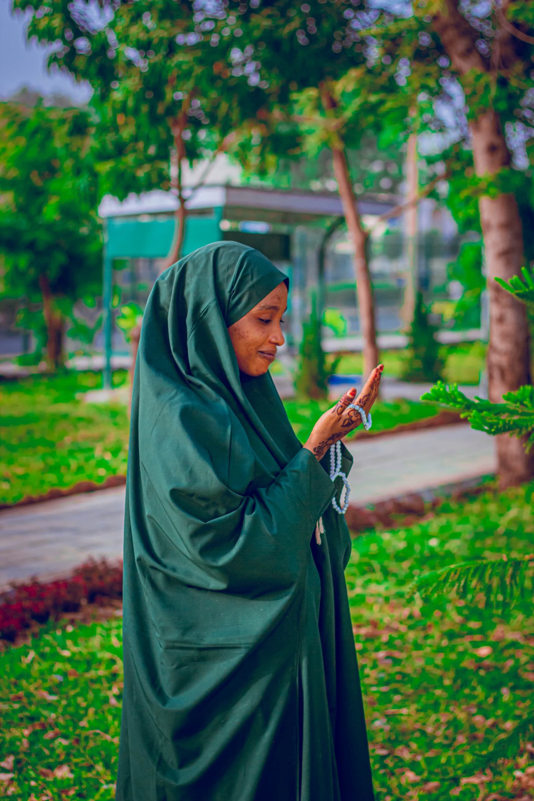 a profile view of a smiling African woman in a deep green burka who is holding her right hand up that's wrapped in blue prayer beads